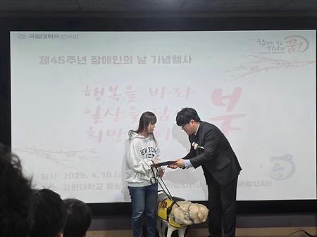 장애인의 날 포상 대상자 학생과 안내견이 센터 선생님으로부터 상장을 건네받고 있다.